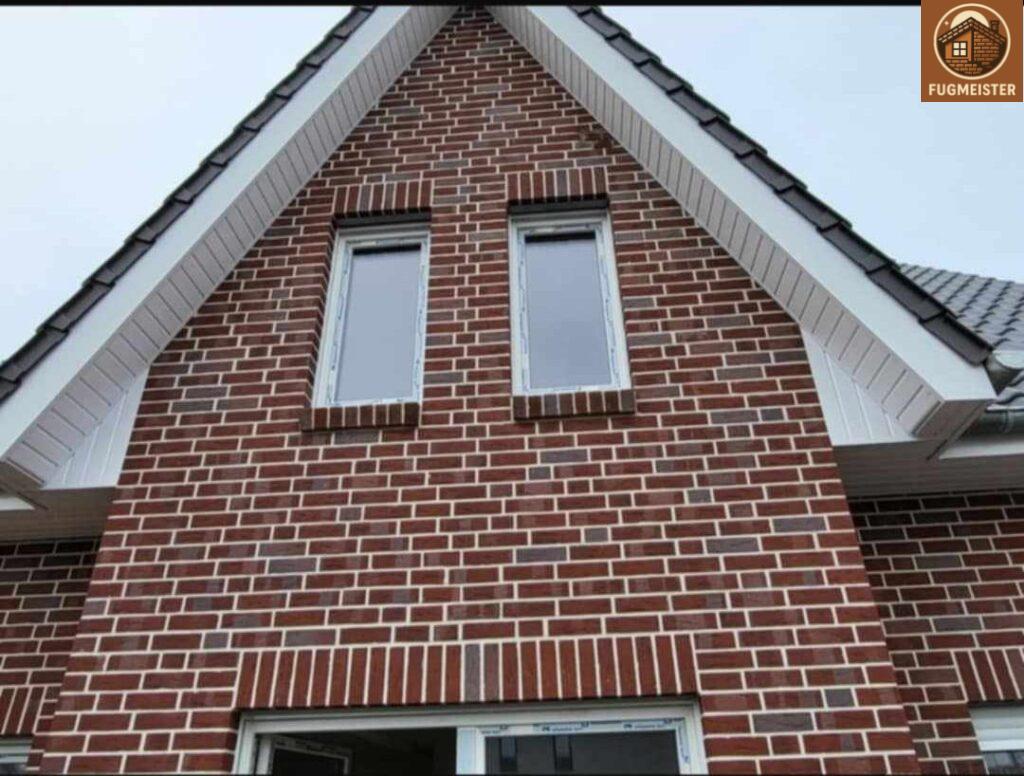 Fassadenansicht eines Wohnhauses mit hochwertiger Klinkerarbeit und präziser Fensterintegration.