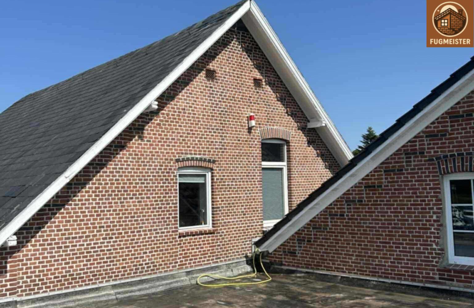 Fugmeister-Fassade: sauber verfugter Klinkergiebel mit zwei Fenstern und präzisem Dachanschluss.
Fugmeister Ziegelarbeit — Giebelwand mit exakten Fugen und Anschluss an das Nebendach im sonnigen Innenhof.