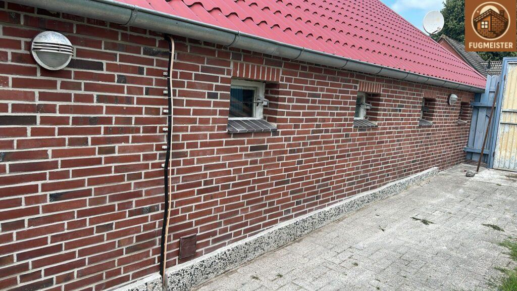 Backsteinwand mit rotem Metalldach; mehrere kleine Fenster und sichtbare Installationsleitung.