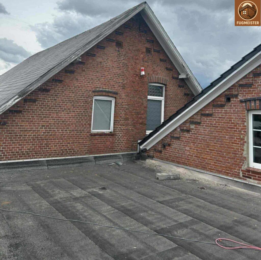 Giebel eines Klinkerhauses mit Flachdach-Terrasse und Dachanschluss, bewölkter Himmel.