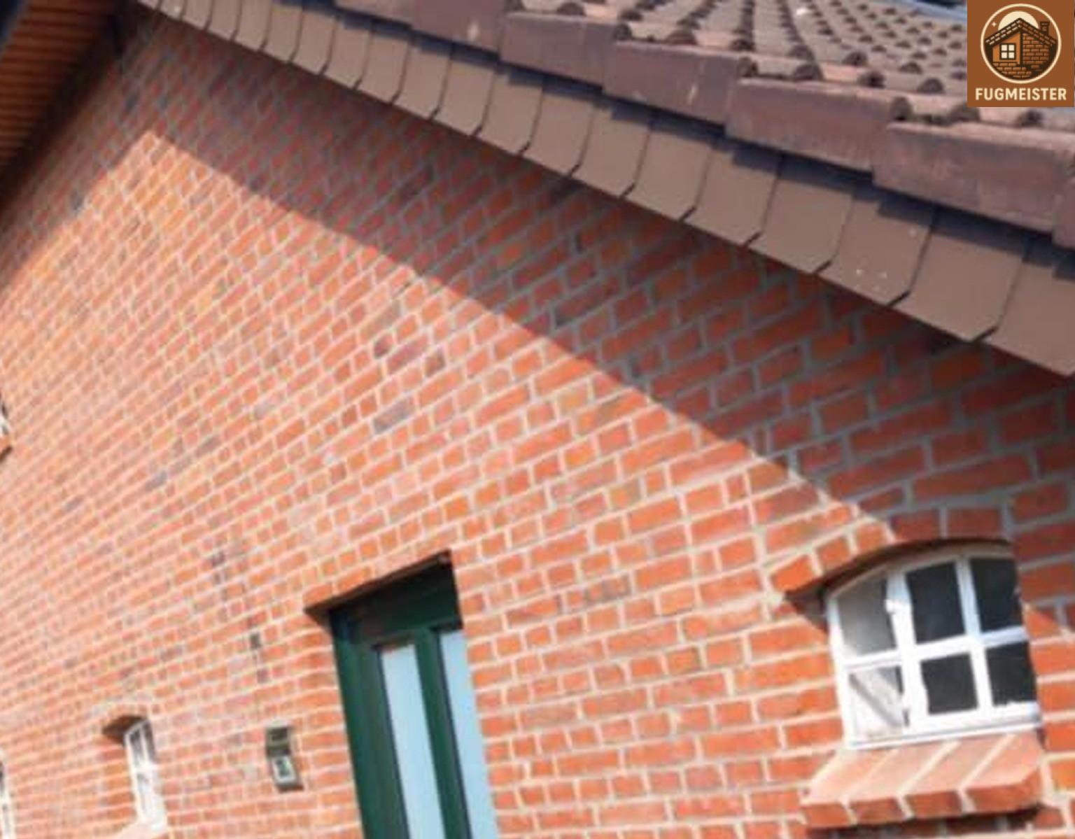 Ziegelfassade mit schrägem Dach, Segmentbogenfenster und grüner Tür; saubere Fugmeister-Arbeit.
